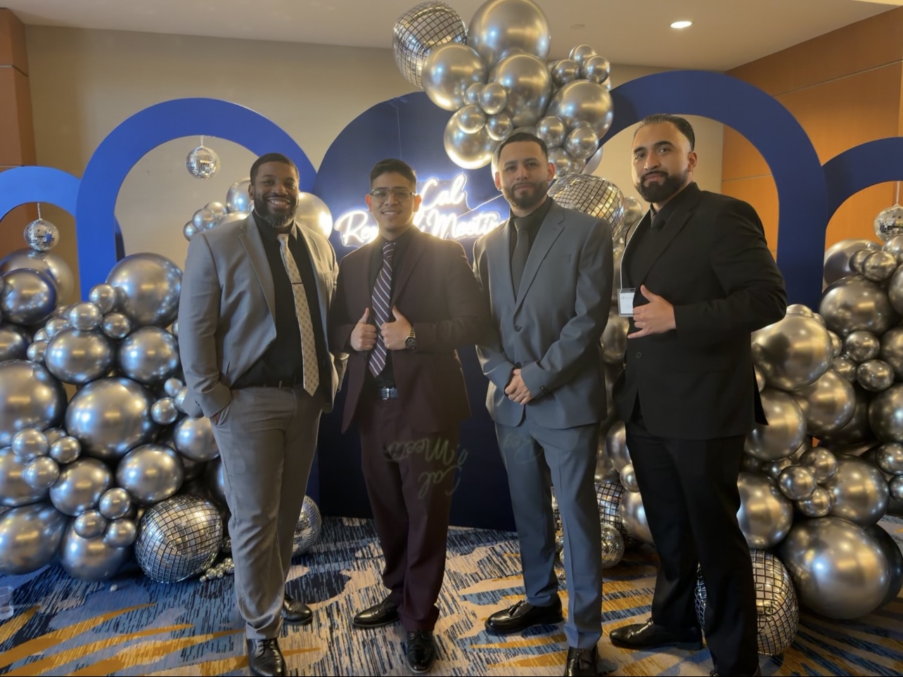 Infinite Reign Solution team members in professional suits at a conference with blue and silver decor